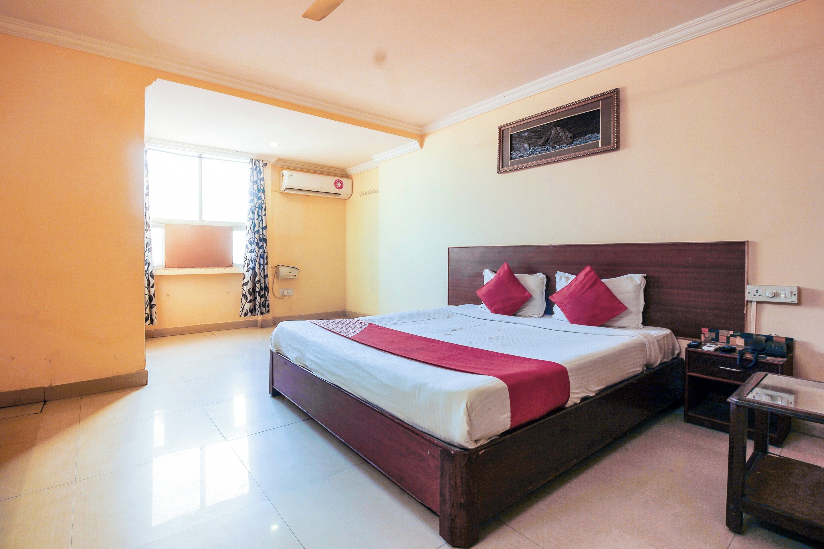 Habitación de hotel con cama, mesita de noche y ventana con cortinas.