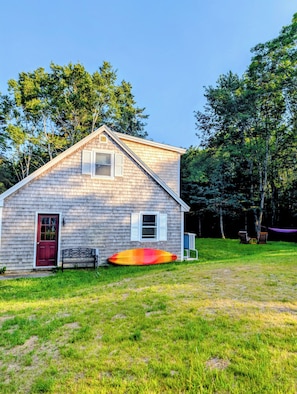 A wooden house with a red door, a bench, and a surfboard in the yard. - Cozy Coastal Studio Cottage a short walk to Pemaquid Beach (Bristol)
