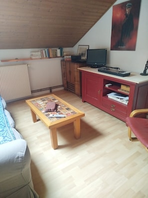 A cozy living room with a wooden coffee table, a red cabinet, a television, and a bookshelf. - A large, unique townhouse, 15 minutes from Puy du Fou (Mortagne-sur-Sèvre)