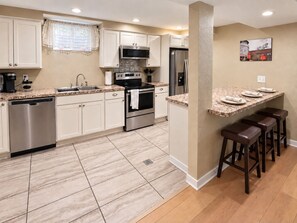 A modern kitchen with a dishwasher, stove, microwave, refrigerator, and a bar area with stools. - Upscale Two-Suite Denver Retreat - Sleeps 11 (Denver)