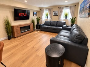 A living room with a flat-screen TV, leather sofa, wooden flooring, and potted plants. - Upscale Two-Suite Denver Retreat - Sleeps 11 (Denver)