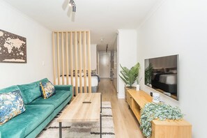 A modern living room with a green sofa, wooden coffee table, and a TV mounted on the wall. - Newlands Peak Studio Apartment (Cape Town)