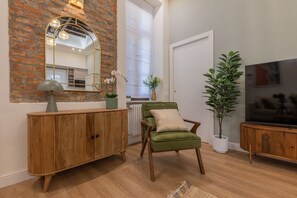 A living room with a brick wall, a green armchair, a wooden cabinet, a mirror, a potted plant, and a television. - San Francesco Boutique House by Wonderful Italy (Turin)
