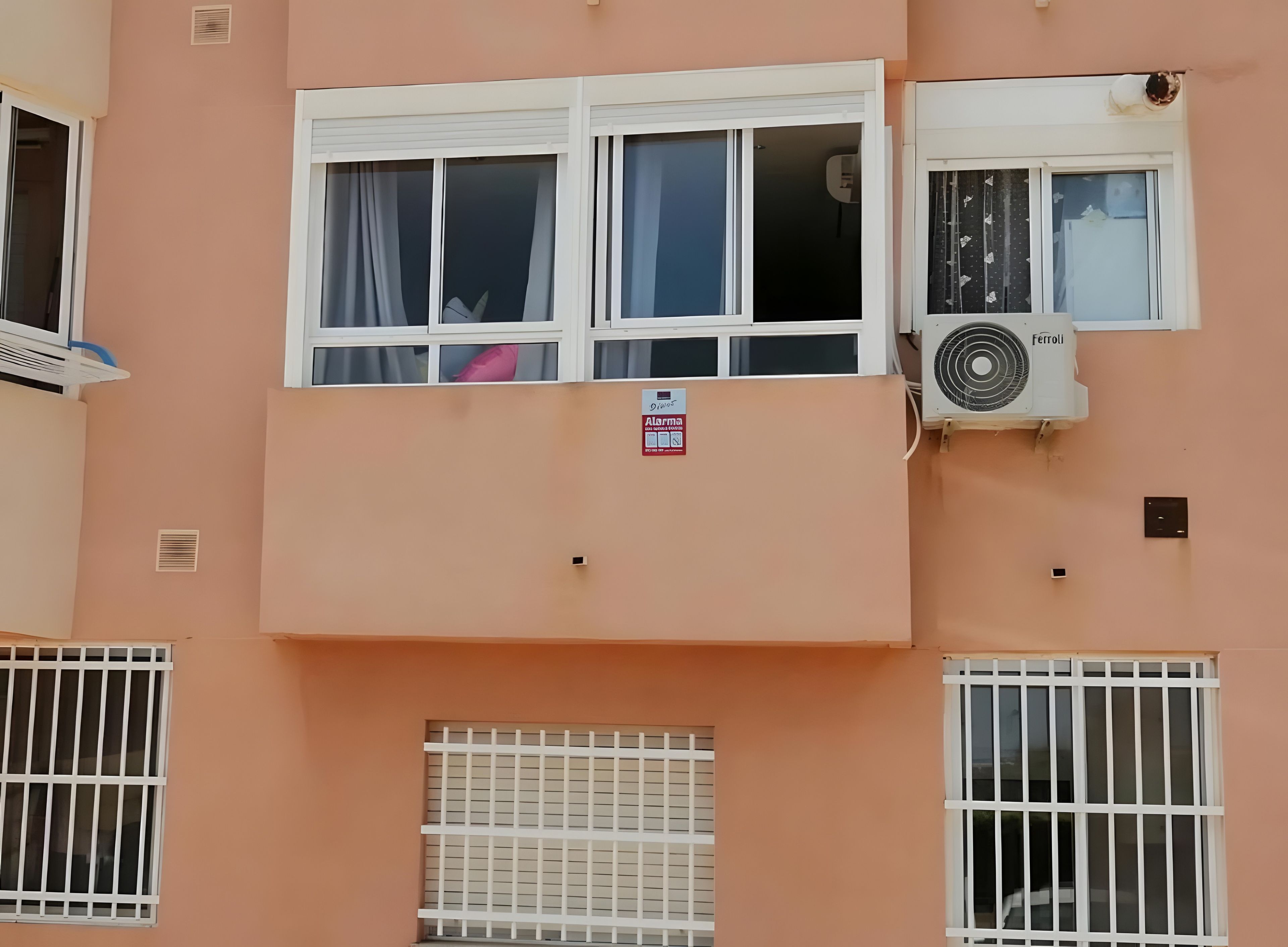 A building facade with multiple windows, some with curtains, and an air conditioning unit.