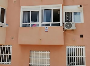 Une façade d’immeuble avec de nombreuses fenêtres, dont certaines sont dotées de rideaux, et un appareil de climatisation.