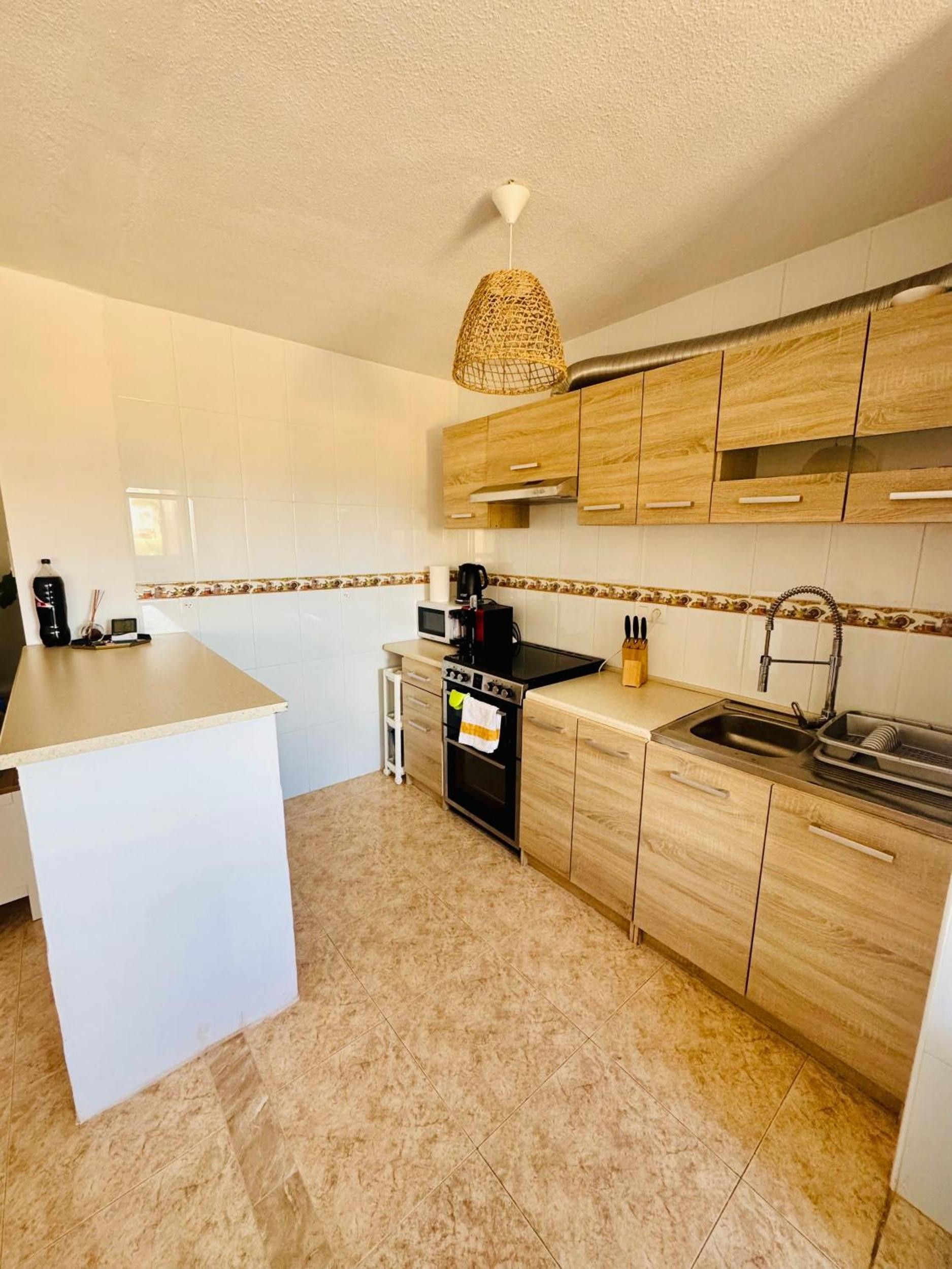 Une cuisine moderne avec des meubles blancs, un îlot central, un four encastré et un luminaire suspendu.