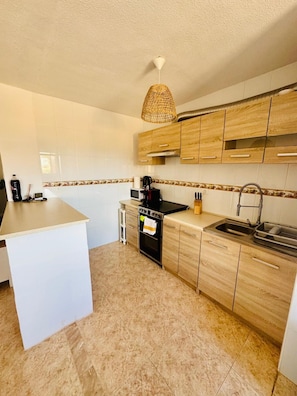 Une cuisine moderne avec des meubles blancs, un îlot central, un four encastré et un luminaire suspendu.