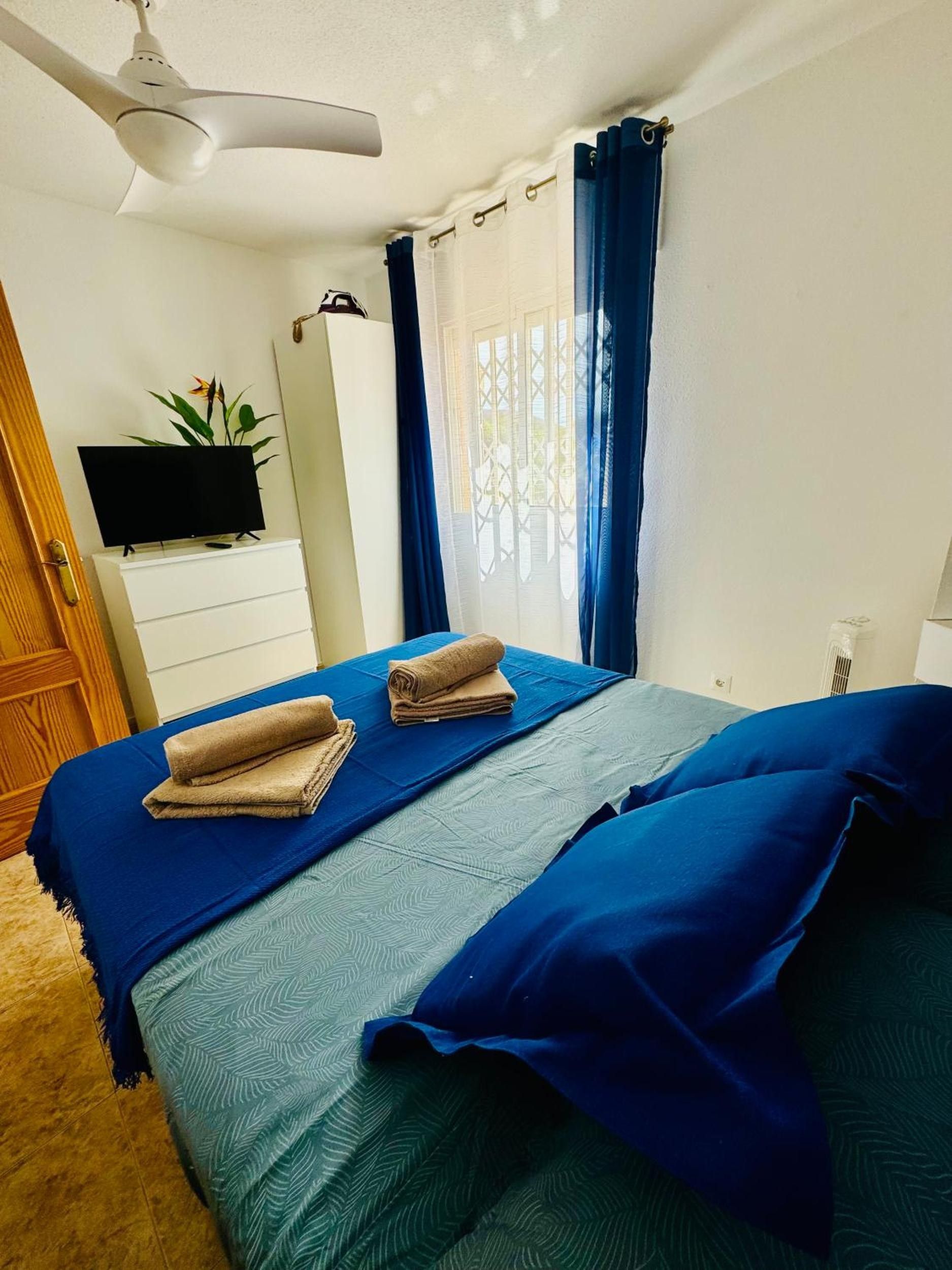 Ein Schlafzimmer mit einem Bett, einem Flachbildfernseher, einem Schminktisch, einem Deckenventilator und einem Fenster mit Vorhängen.