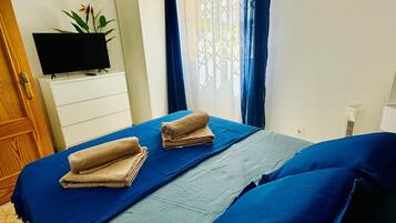 Ein Schlafzimmer mit einem Bett, einem Flachbildfernseher, einem Schminktisch, einem Deckenventilator und einem Fenster mit Vorhängen.