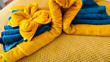 Una cama con un edredón amarillo texturizado, toallas azules y amarillas, y un arreglo decorativo de almohadas.
