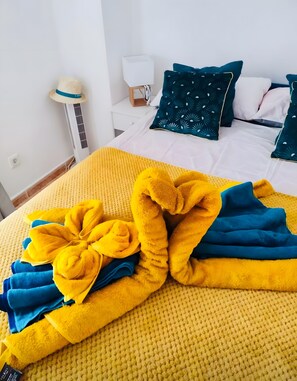 A bed with a yellow textured blanket, blue and yellow towels, and a decorative pillow arrangement.