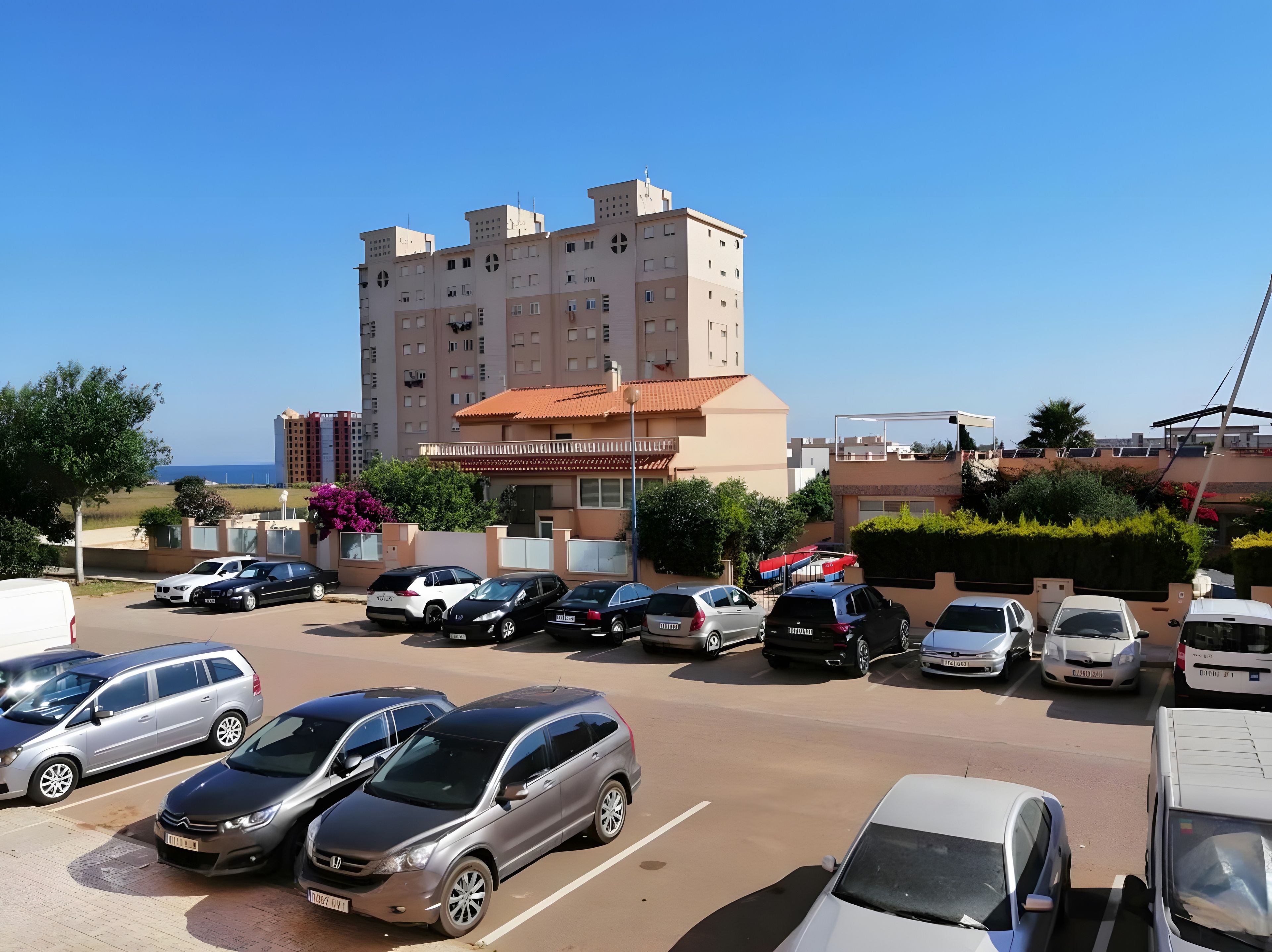 A parking lot with multiple cars and a building with a red roof.