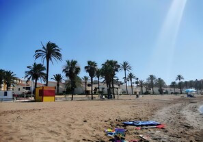 A sandy beach with palm trees, a lifeguard tower, and buildings in the background.