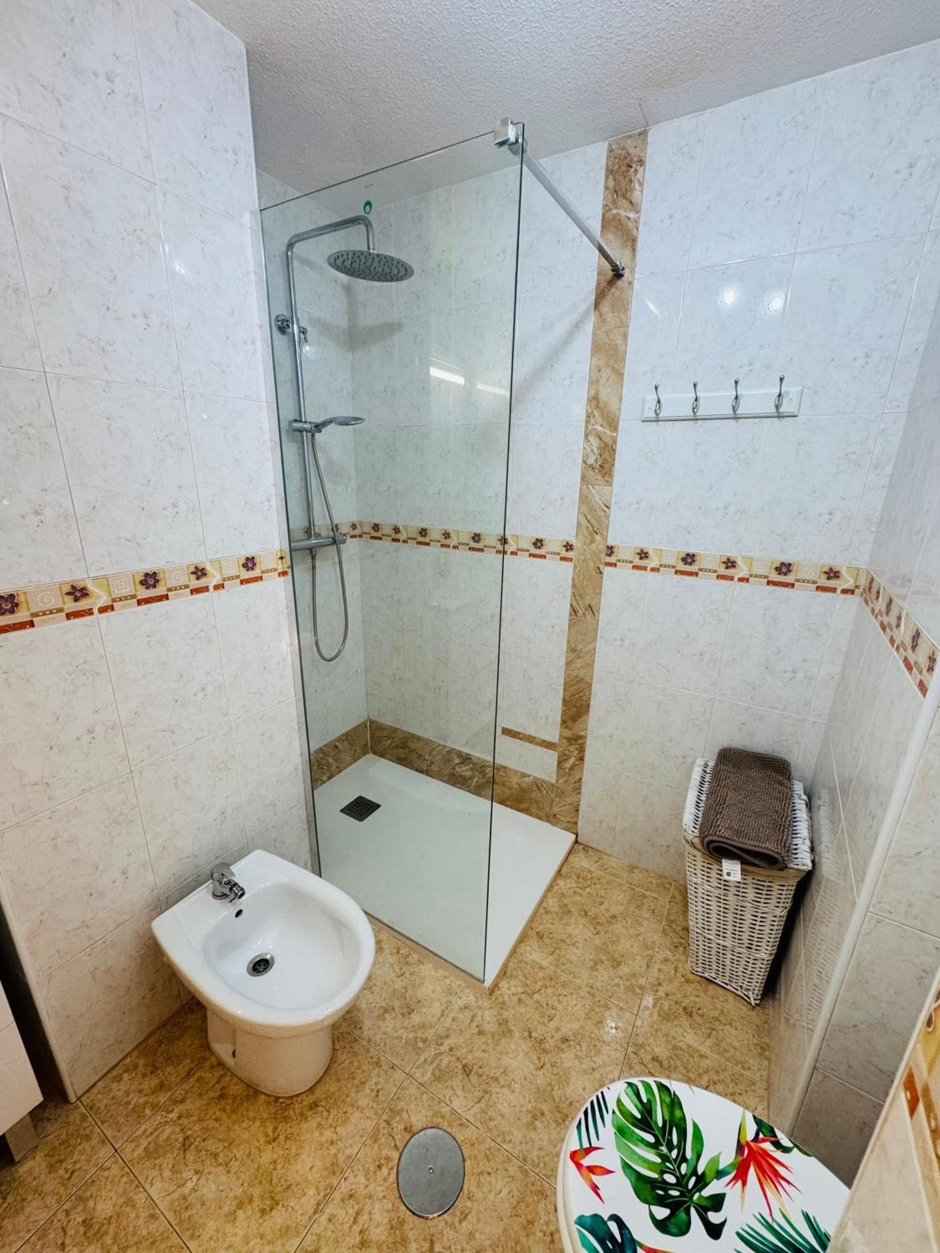 Ein Badezimmer mit einer Duschkabine, einem Waschbecken, einer Toilette und einem kleinen Korbwäscheschrank.