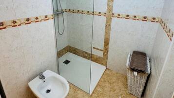 Ein Badezimmer mit einer Duschkabine, einem Waschbecken, einer Toilette und einem kleinen Korbwäscheschrank.