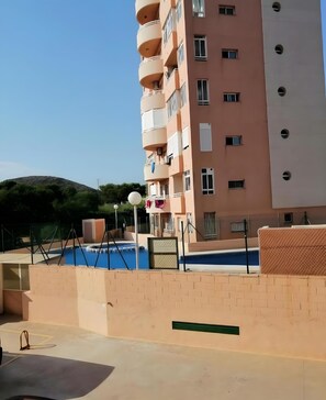 A multi-story residential building with balconies, a swimming pool, and a view of a hilly landscape. - Apartment 'La Manguita' with Shared Pool, Wi-Fi and Air Conditioning (Playa Honda)