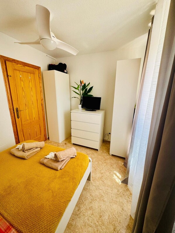 A bedroom with a bed, a white wardrobe, a small desk with a plant, and a ceiling fan. - Apartment 'La Manguita' with Shared Pool, Wi-Fi and Air Conditioning (Playa Honda)