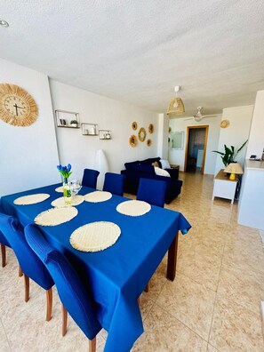 Un coin repas avec une nappe bleue, des sets de table ronds et des chaises recouvertes d’un tissu bleu.