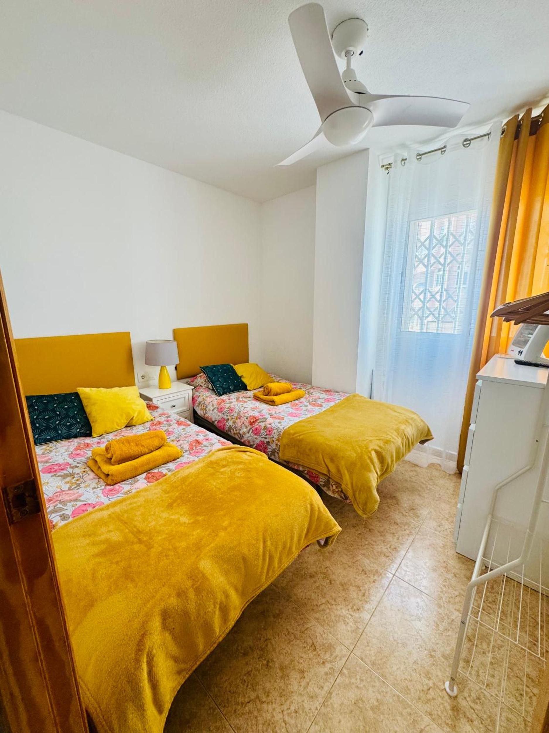 Habitación de hotel con dos camas, un ventilador de techo, una ventana con cortinas y un armario blanco.