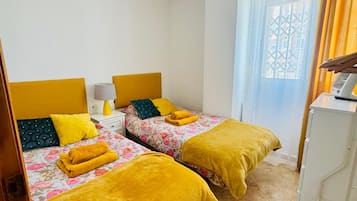 Habitación de hotel con dos camas, un ventilador de techo, una ventana con cortinas y un armario blanco.
