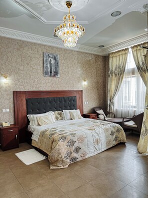 Ein Schlafzimmer mit einem großen Bett, einer Chandelüster, einem Nachttisch, einem Sessel und einem Bild an der Wand.