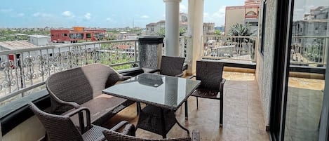 A balcony with wicker furniture, a glass table, and a view of the cityscape.
