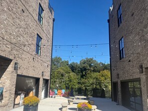 A courtyard with brick buildings, outdoor seating, and string lights. - NEW! Walk Neyland Vintage Vol Theme - 3 master bedroom, rooftop deck w/ Hottub. (Knoxville)