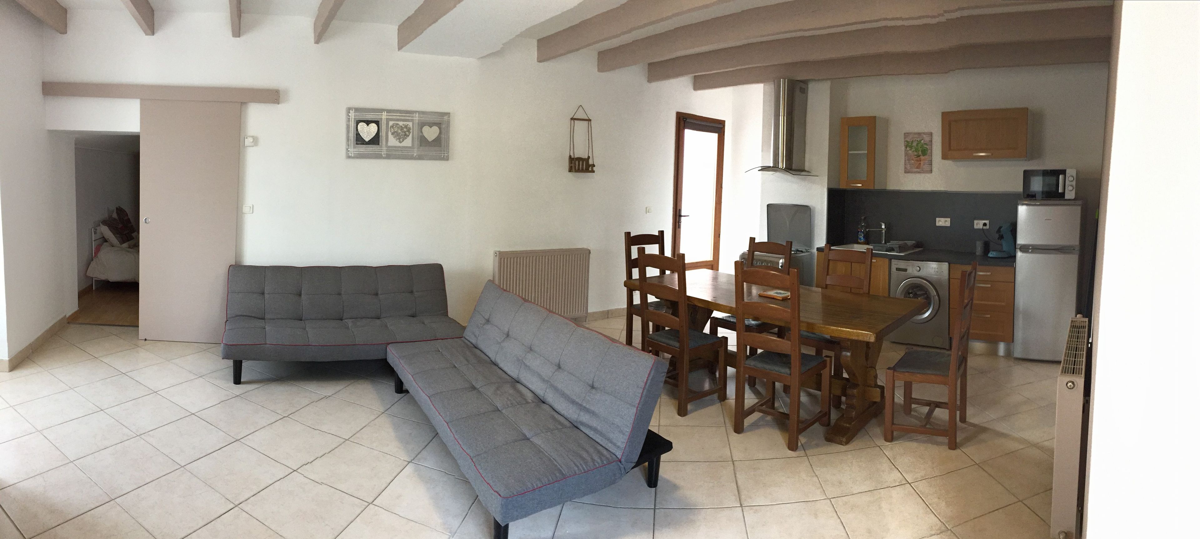 Ein Wohnzimmer mit Sofa, einer Bank und einem Esstisch mit Stühlen. Es gibt eine Küchenzeile mit Kühlschrank und Mikrowelle.