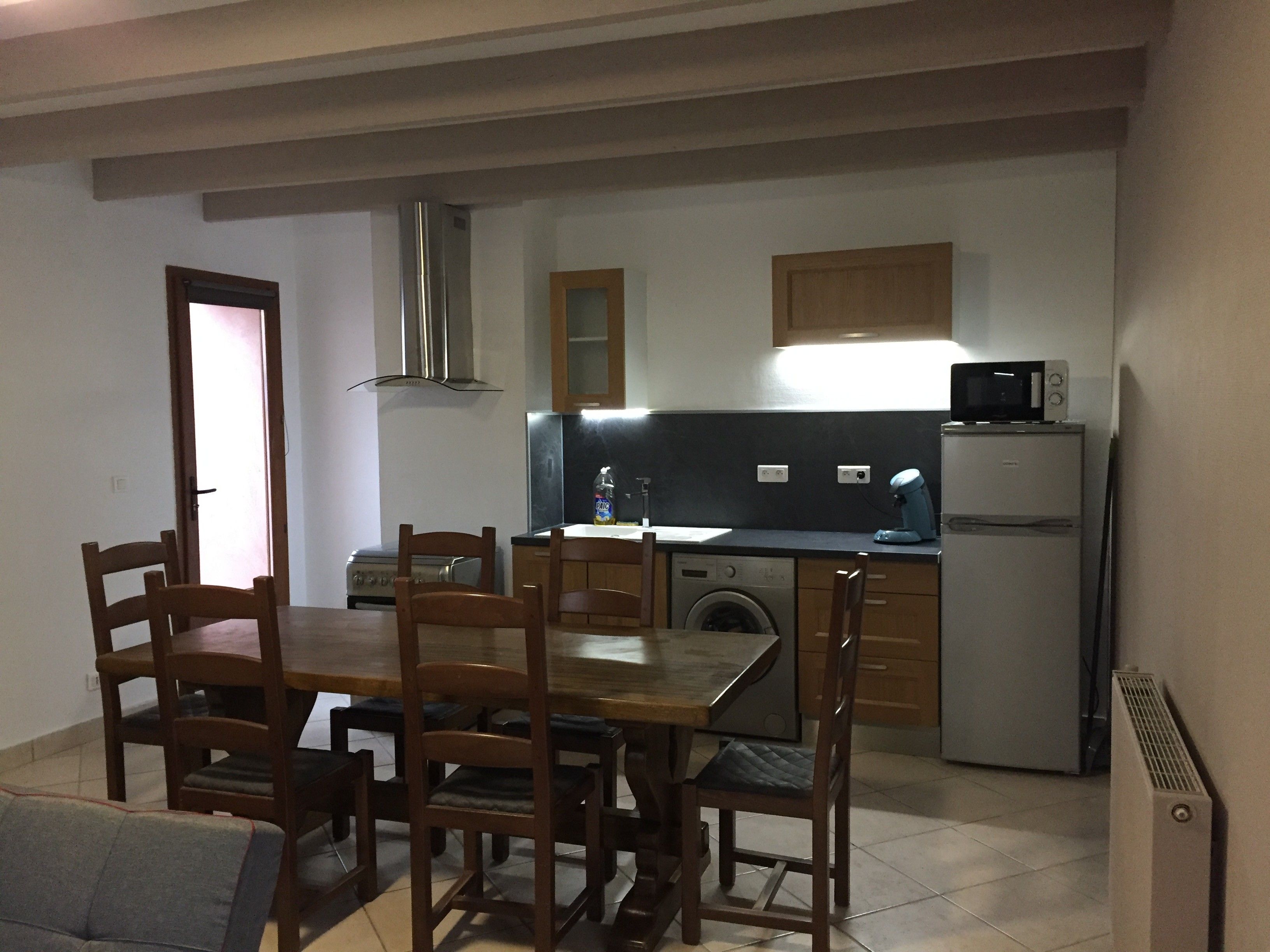 Een functionele keuken met eethoek, inclusief een tafel, stoelen, een wasmachine, een magnetron en een koelkast.