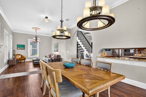 Een ruime eethoek met een houten tafel en stoelen, een kroonluchter en uitzicht op de keuken.
