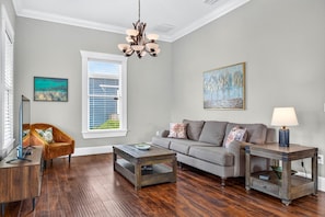 A living room with a sofa, two coffee tables, a chair, a TV, and artwork on the walls. - 4BR Historic Ybor Home | Sleeps 9 | 3.5 Baths (Tampa)