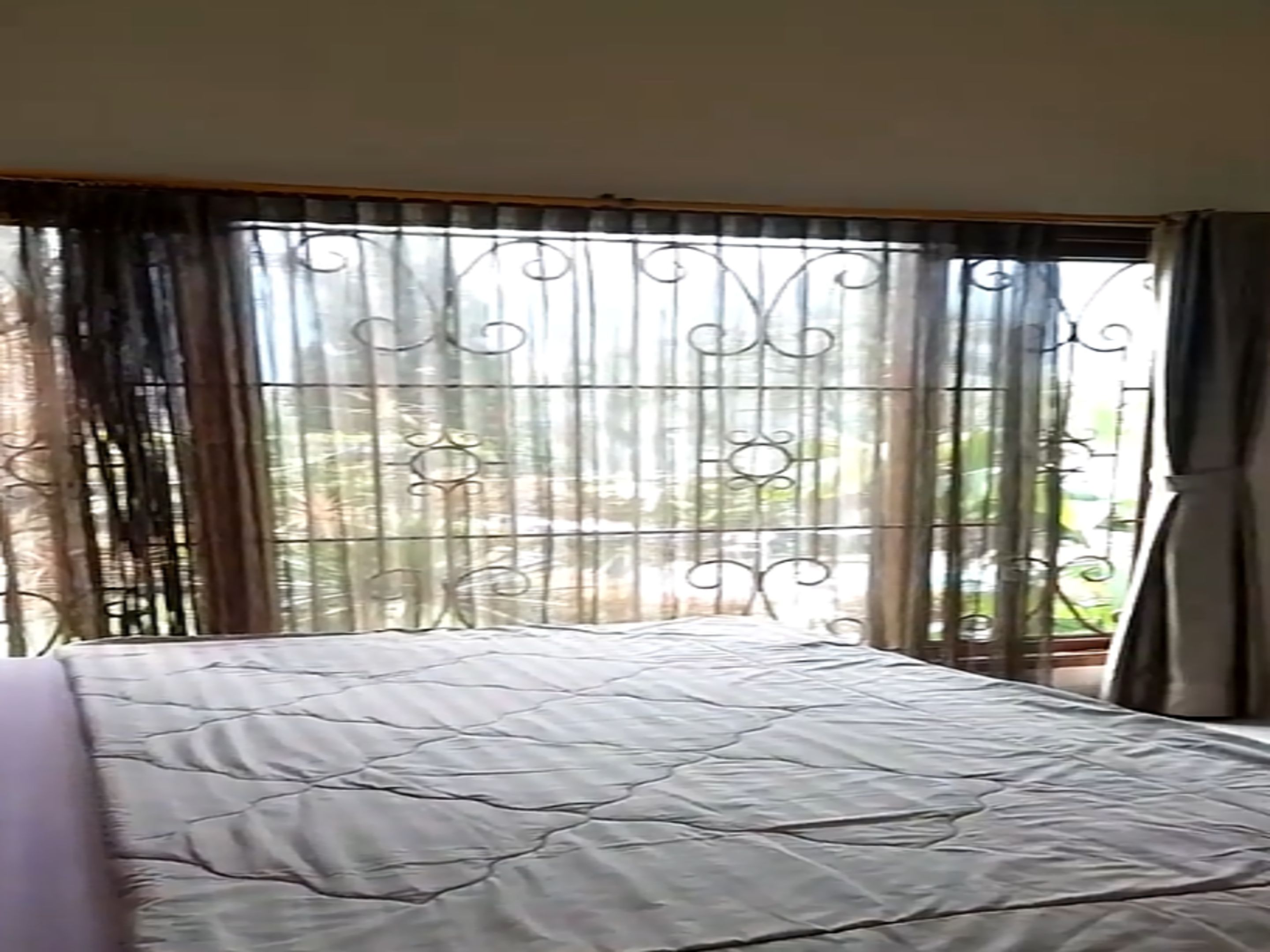 A room with a bed, curtains, and a view of greenery outside.