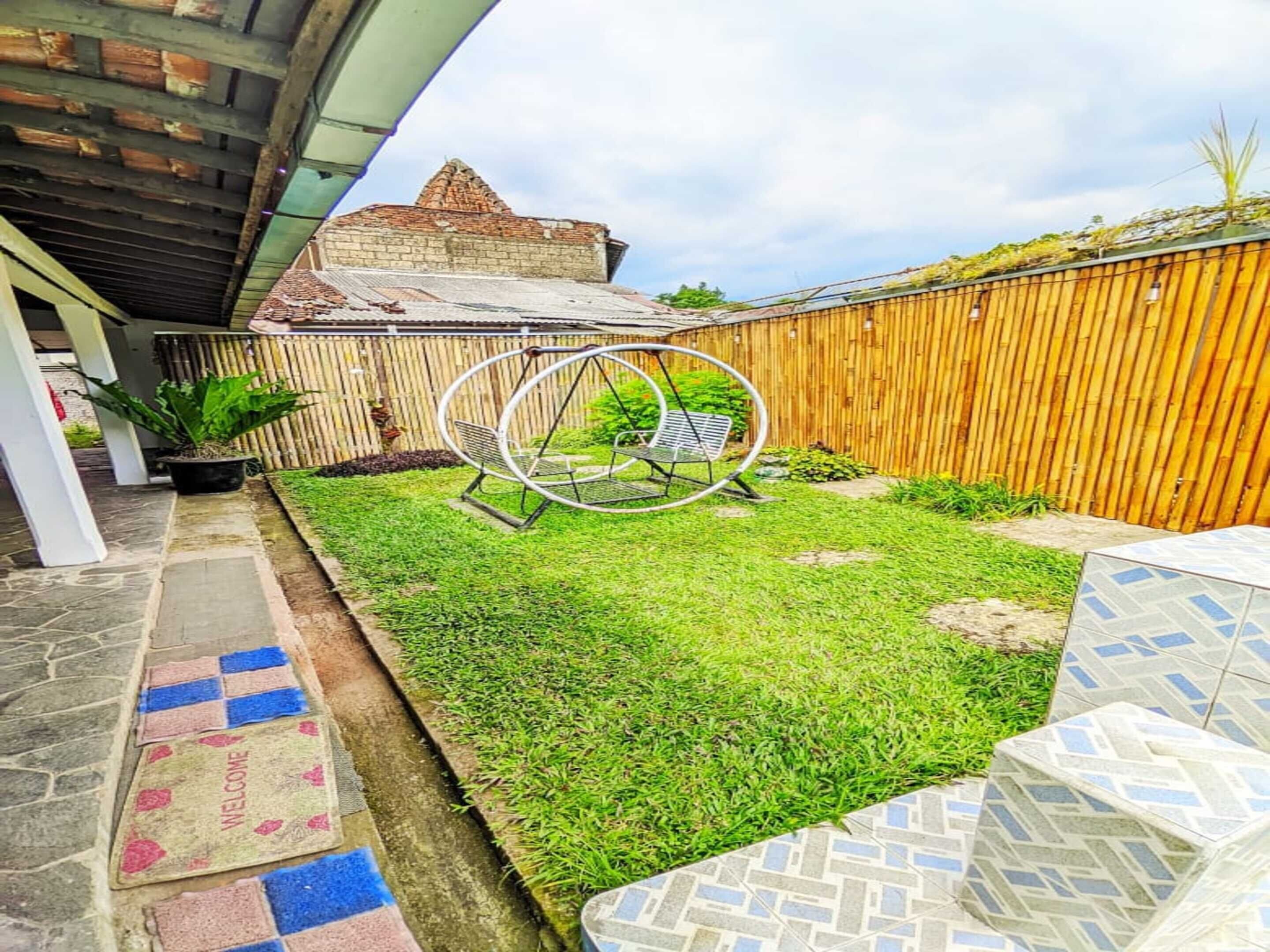 A backyard with a swing set, a wooden fence, and a building with a sloped roof.