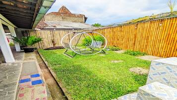 A backyard with a swing set, a wooden fence, and a building with a sloped roof.