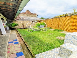 A backyard with a swing set, a wooden fence, and a building with a sloped roof. - Cozzy Villa Bintang Batulayang (bOGOR)