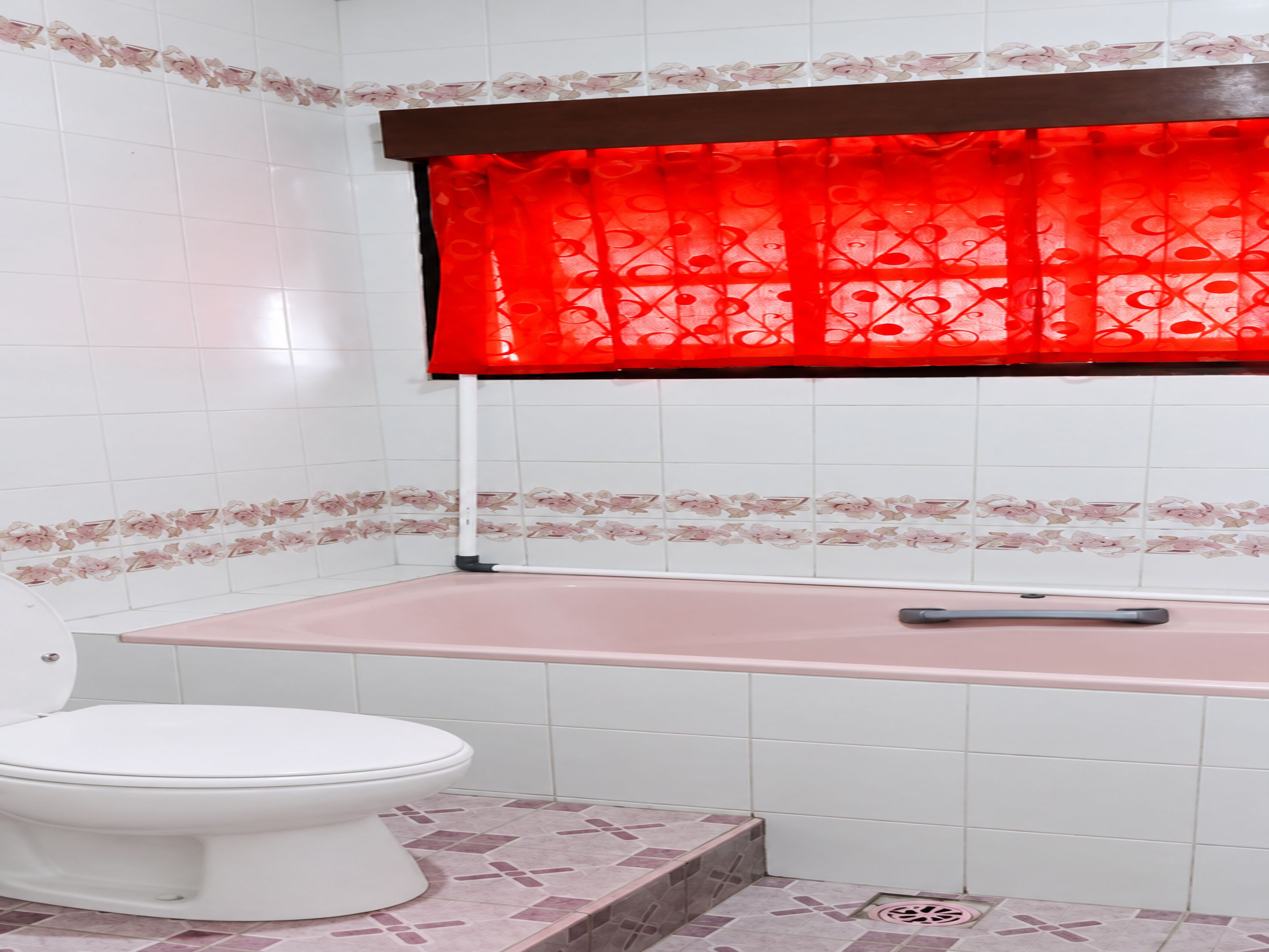 A bathroom with a toilet, a shower area, and a window with a red curtain.