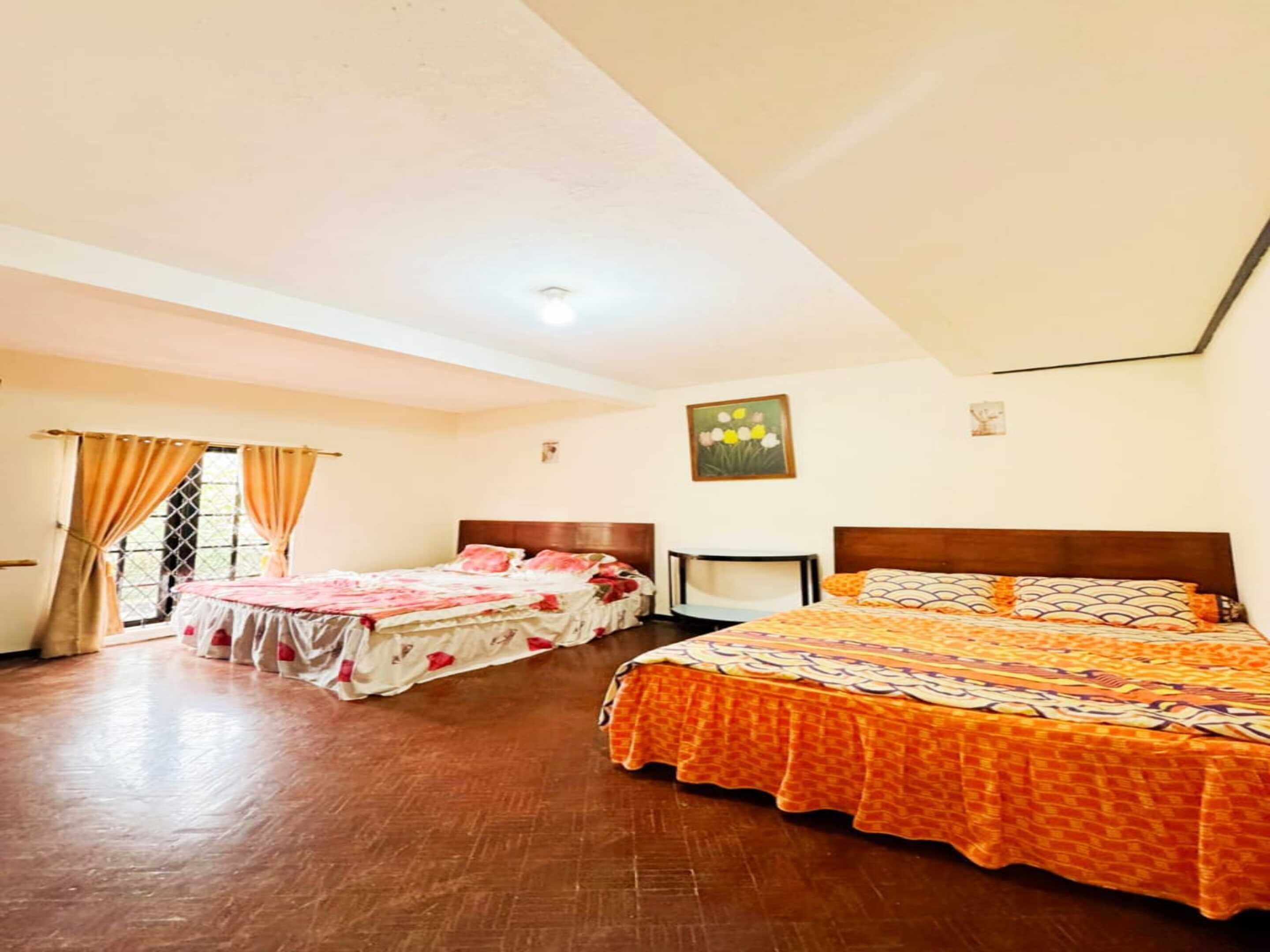 A hotel room with two beds, a wooden floor, and a window with curtains.