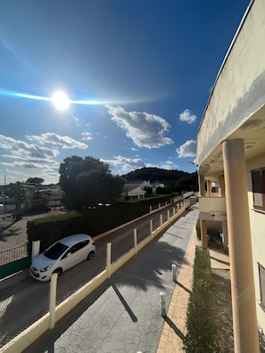 A paved pathway with a white car parked on the side, leading to a building with a flat roof and a visible entrance.