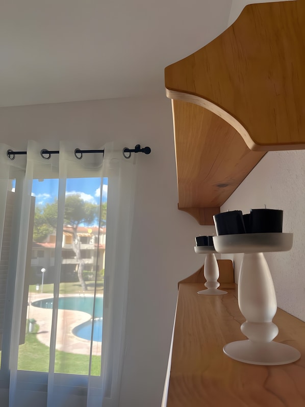 A room with a view of a swimming pool, a wooden ceiling, and a white table with black objects on it.