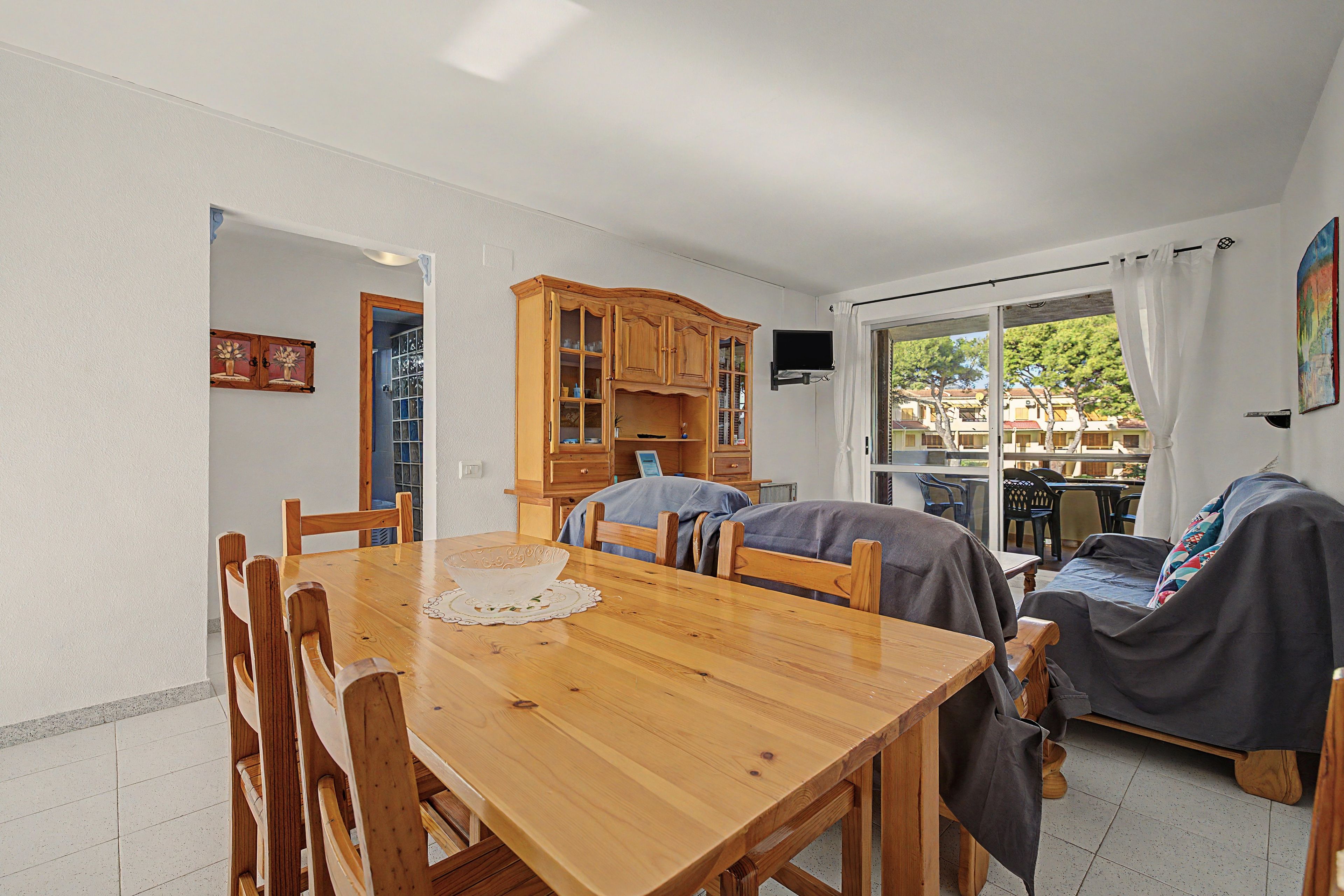 Un comedor con mesa y sillas de madera, una cocina con armarios de madera y vista a través de una puerta de cristal.