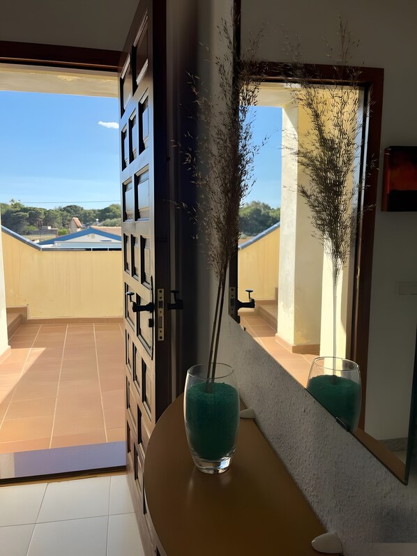 A room with a view of a building and trees, a door with a handle, and a vase with a plant.