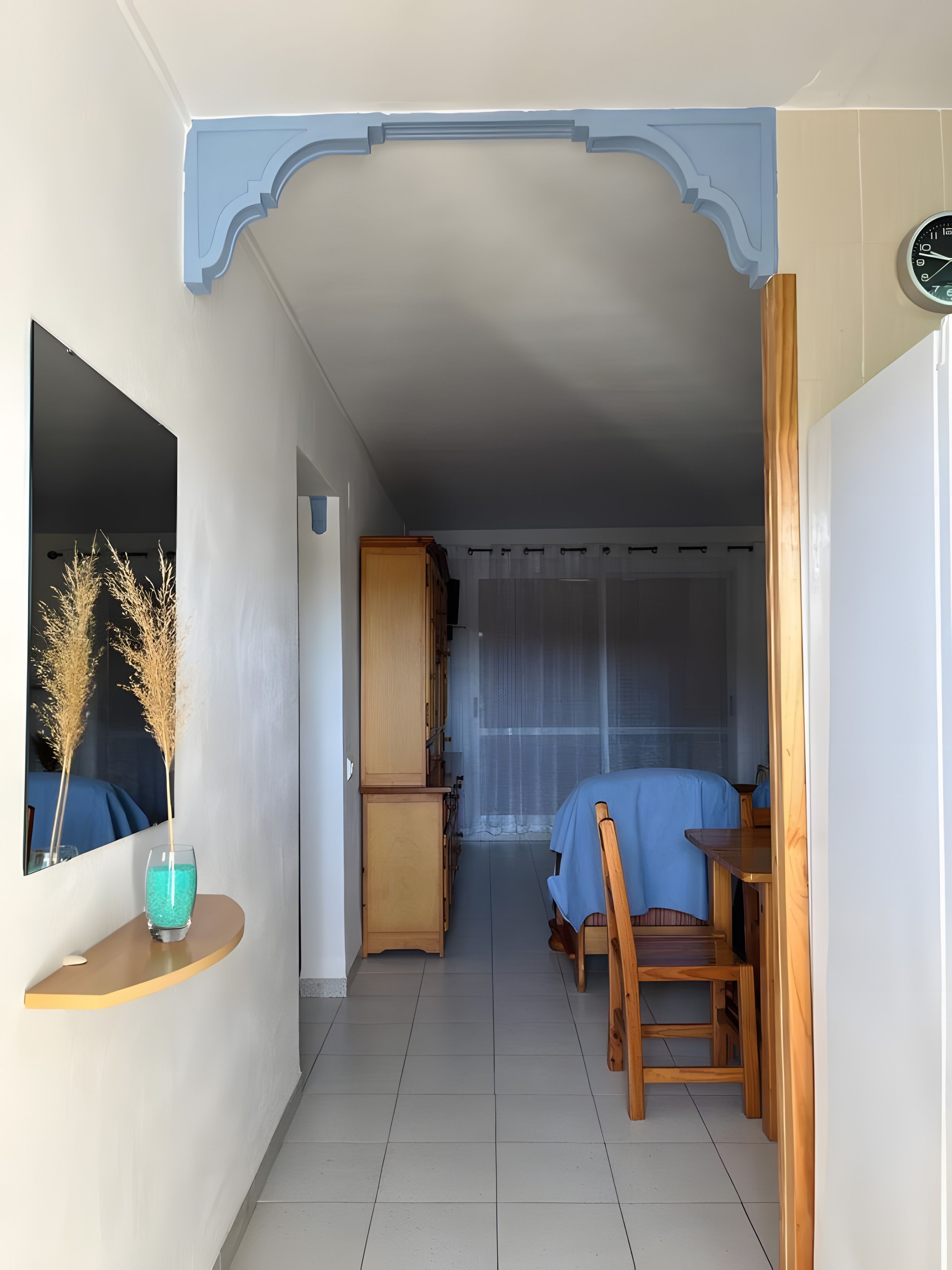 Una habitación con cama, un armario de madera, una mesita con mantel azul y un espejo adornado con plantas.