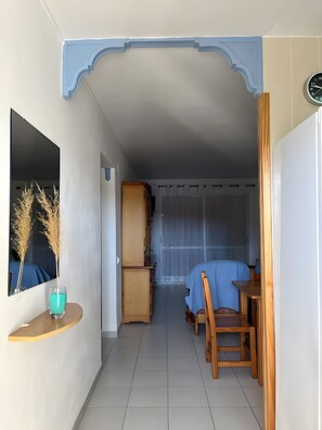 Quarto com cama, um armário de madeira, uma mesa pequena com toalha azul e um espelho com plantas decorativas.