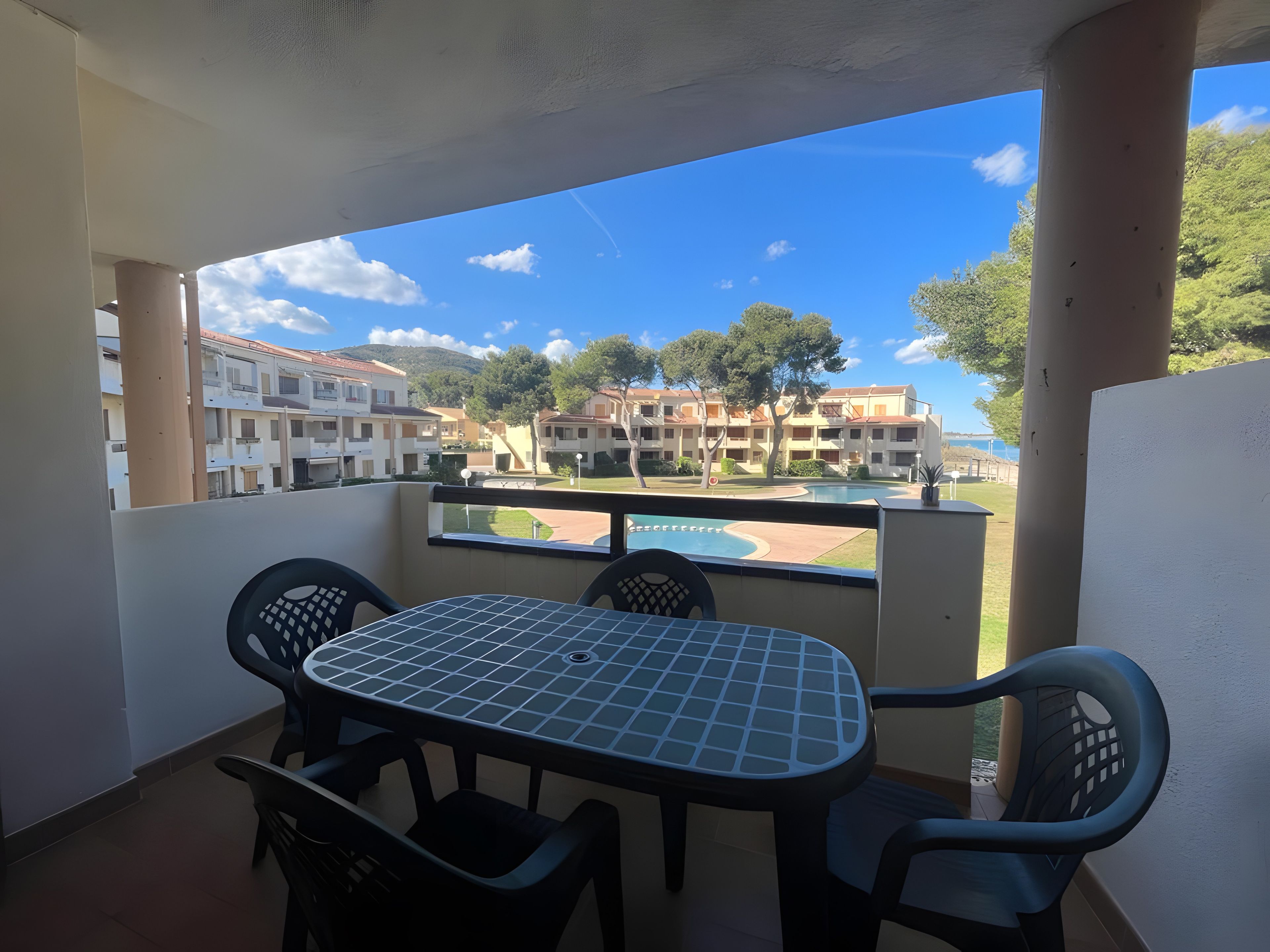 A balcony with a table and chairs, overlooking a pool and buildings.