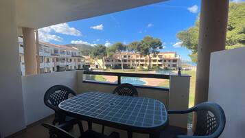 A balcony with a table and chairs, overlooking a pool and buildings.