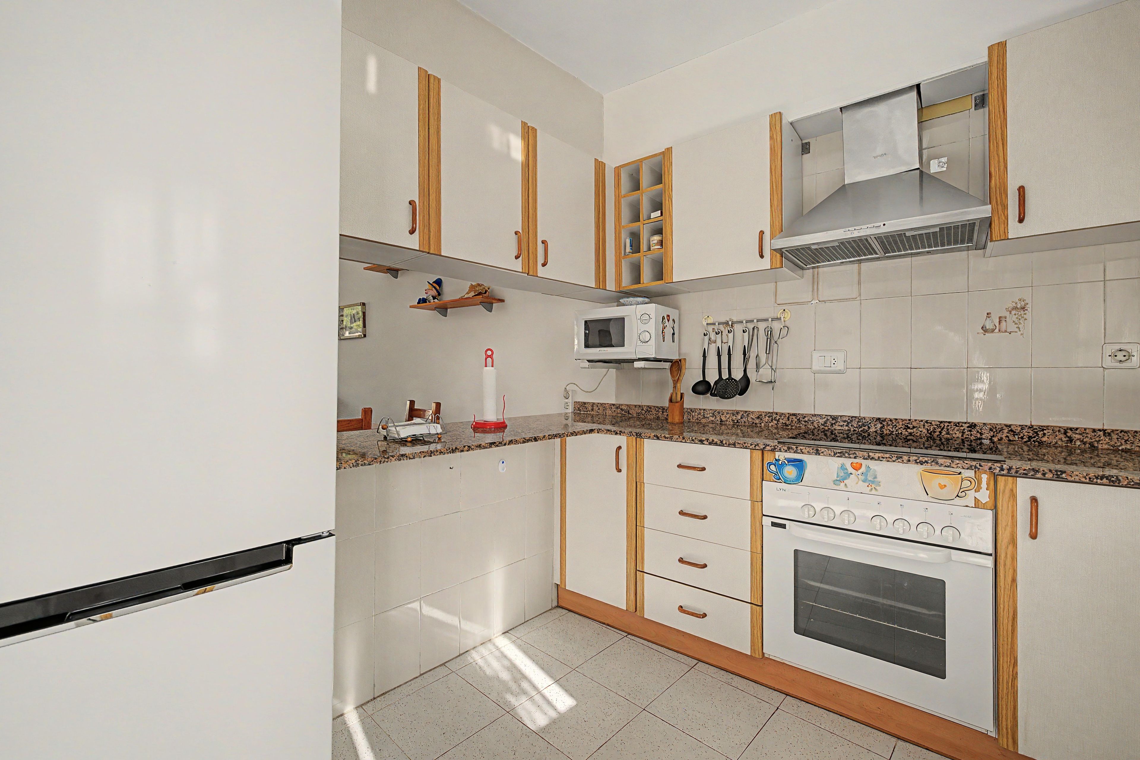 Une cuisine avec des meubles blancs, un four à micro-ondes, une cuisinière et un plan de travail en bois.