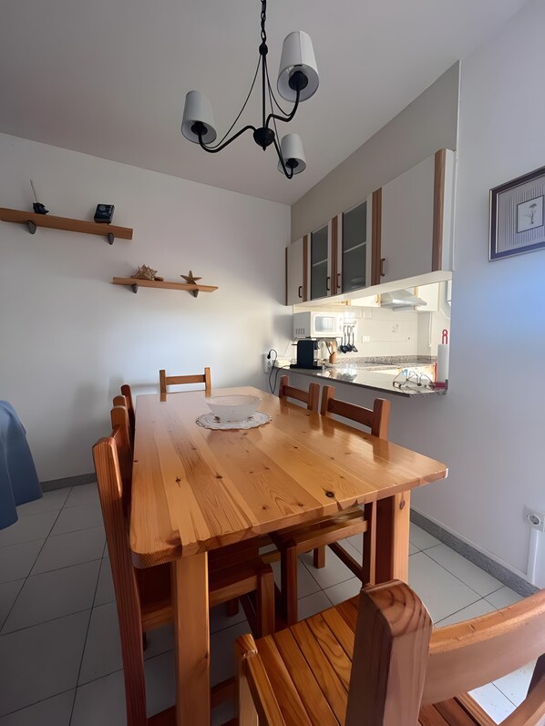 Un comedor con mesa y sillas de madera, una araña y una cocina al fondo.