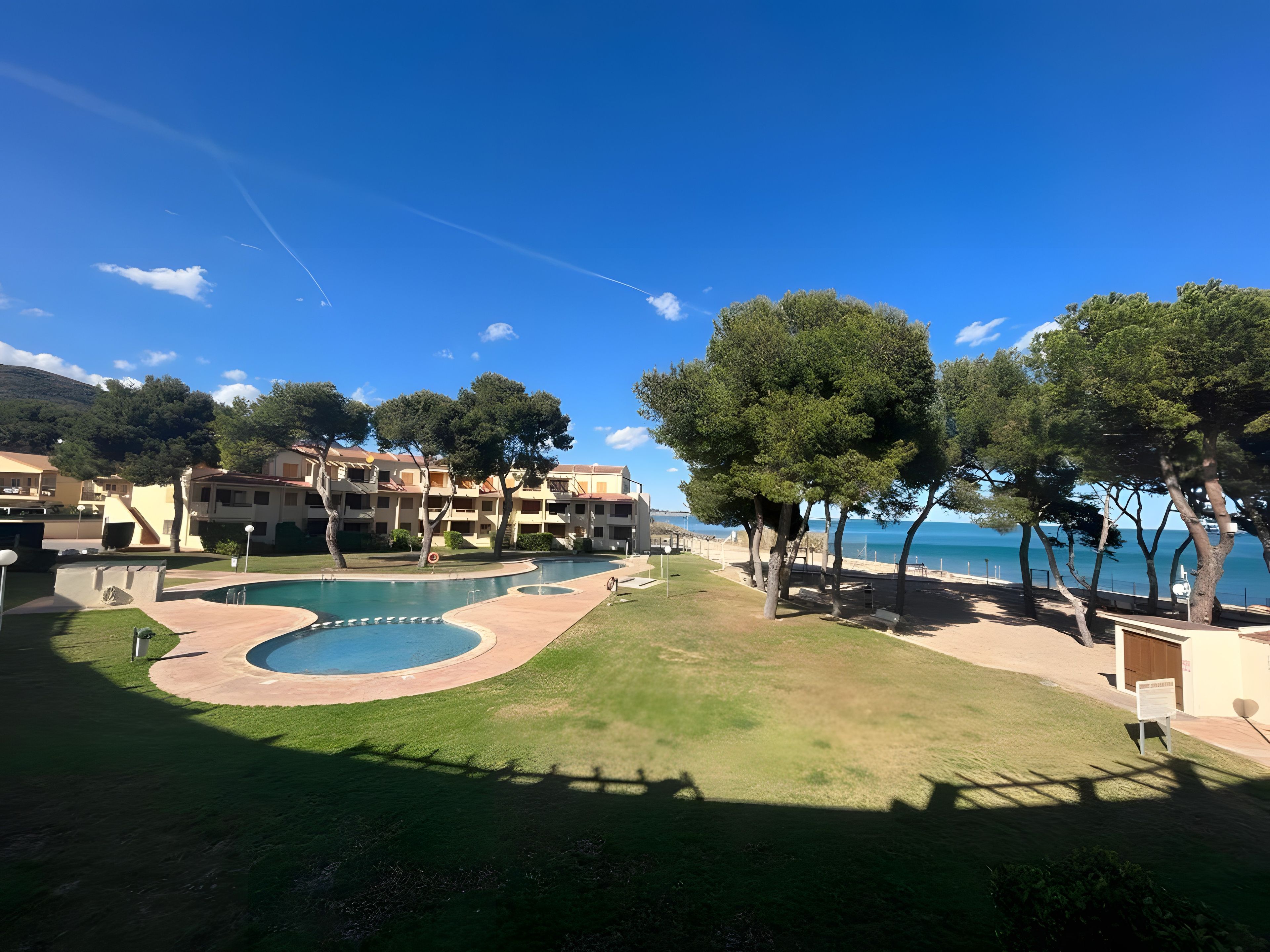 Een resort met een zwembad, bomen en uitzicht op zee.