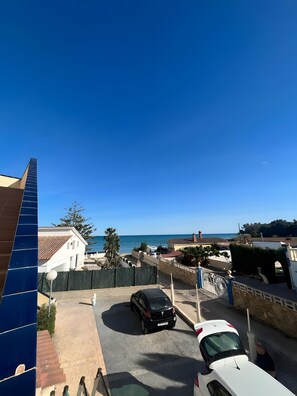 Zona residencial con vista despejada al mar, un coche negro estacionado en la entrada y un coche blanco en primer plano.