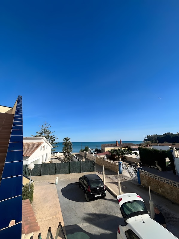 Área residencial com vista ampla para o mar, um carro preto na entrada e um carro branco em primeiro plano.